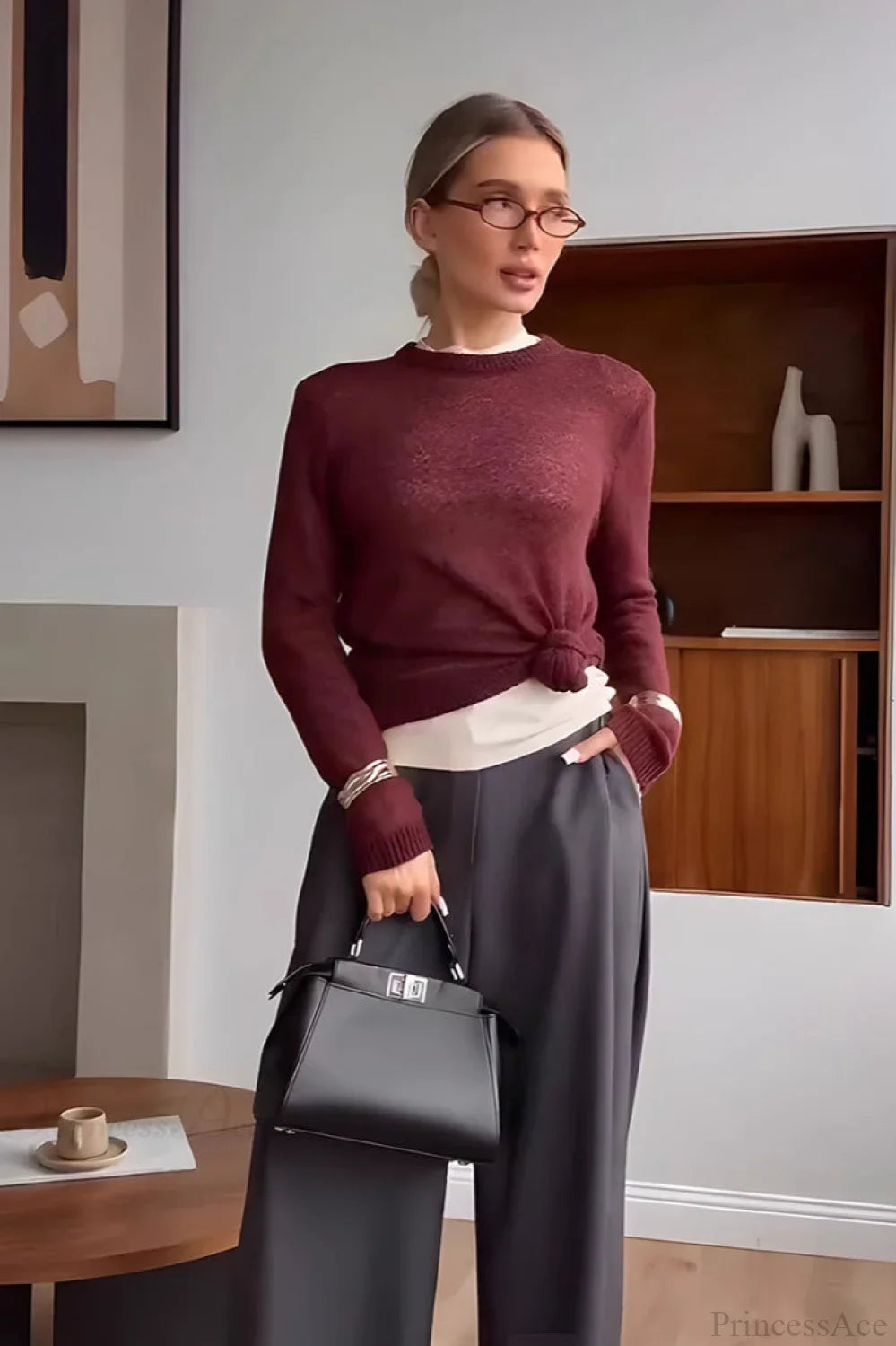 Selena Dark Red crewneck sweater knotted at the hem over a white layer with gray wide-leg trousers.