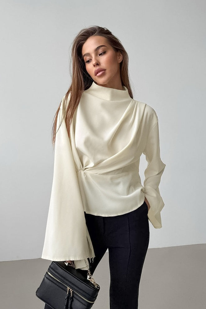 Selene Apricot draped mock neck blouse with flared sleeves styled with black pants and a black handbag.