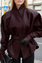Serena Red faux leather belted jacket shown outdoors with a structured high collar, belted waist, long sleeves, and peplum-style shape