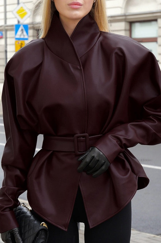Serena Red faux leather belted jacket shown outdoors with a structured high collar, belted waist, long sleeves, and peplum-style shape