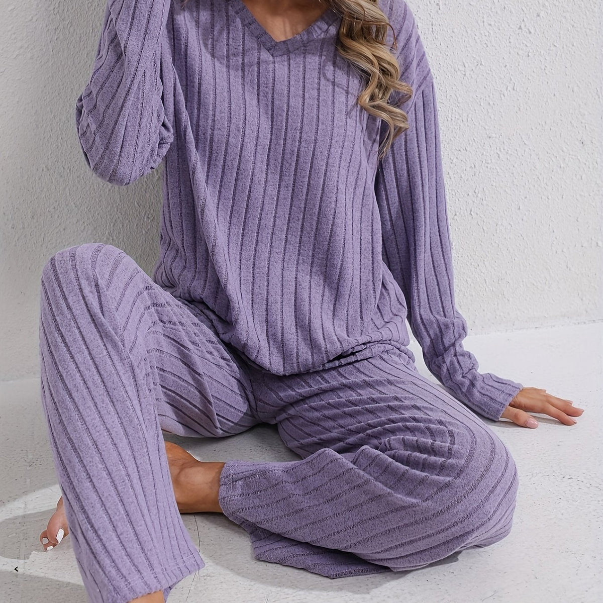 Sloane Purple ribbed two-piece lounge set with a V-neck long-sleeve top and matching wide-leg pants shown in a relaxed seated pose