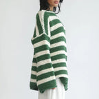 Side view of the Solange Sweater Chunky-Knit Striped in green, showcasing the green and white horizontal stripes, round neckline, long sleeves, chunky knit texture, and oversized fit. Designed by Bella Hudson.