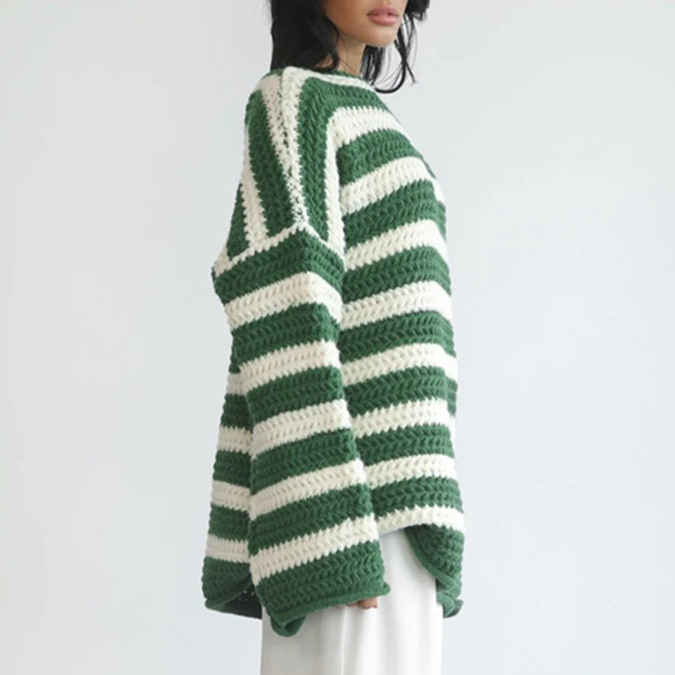 Side view of the Solange Sweater Chunky-Knit Striped in green, showcasing the green and white horizontal stripes, round neckline, long sleeves, chunky knit texture, and oversized fit. Designed by Bella Hudson.