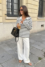 Sophie White striped polo shirt in a full-body look with white linen-style trousers and tan sandals.