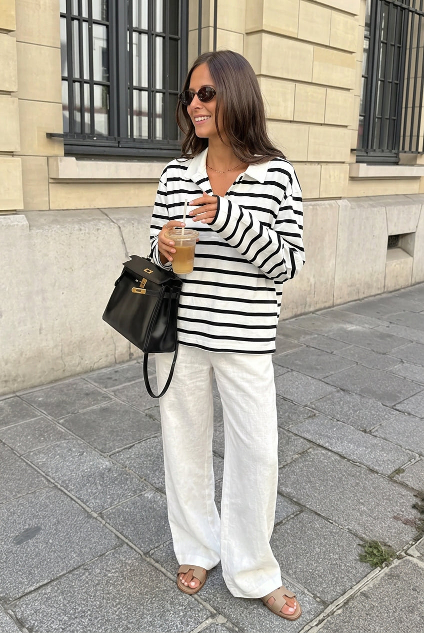 Sophie White striped polo shirt in a full-body look with white linen-style trousers and tan sandals.
