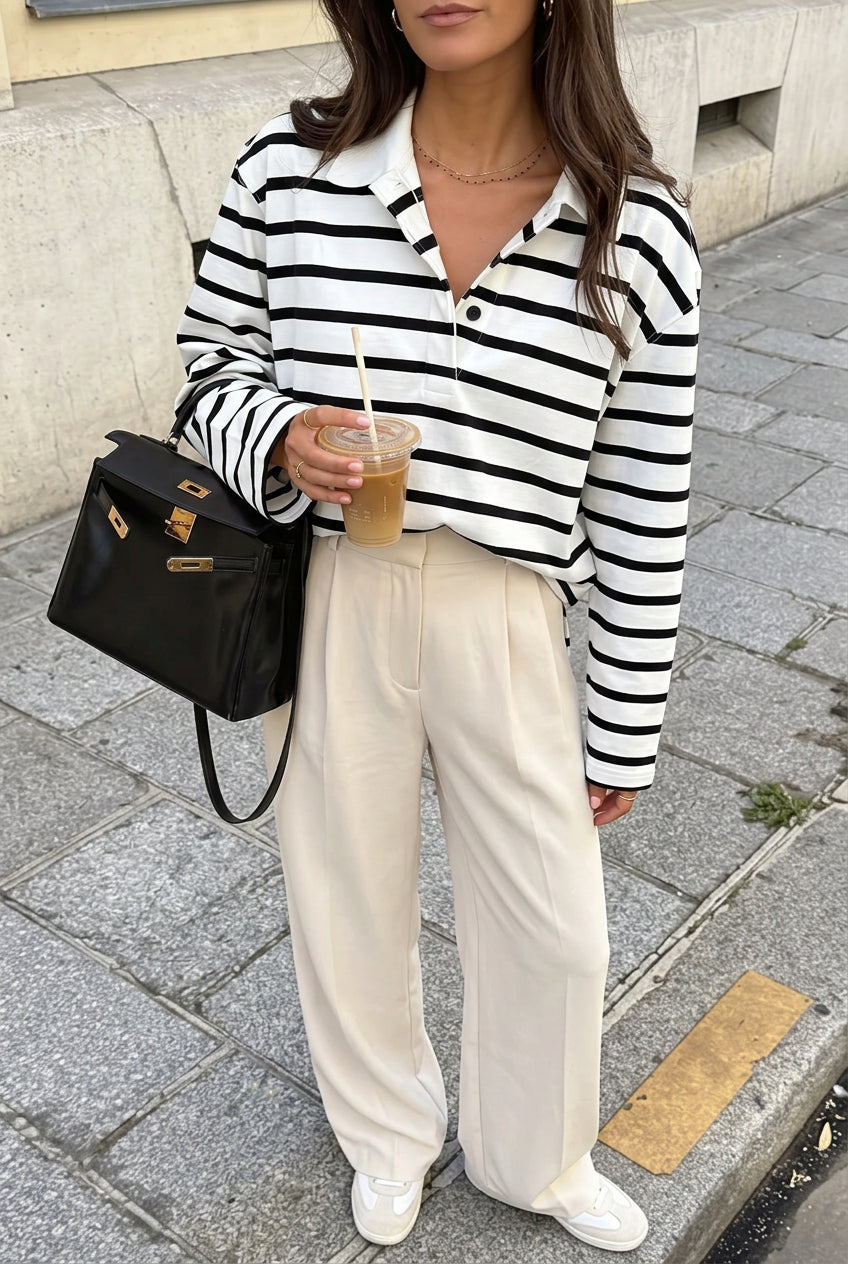 Sophie White striped polo shirt styled with cream pleated trousers, showing the button placket and relaxed fit.