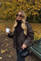 Tessa Brown faux suede jacket styled over a dark turtleneck with a faux shearling collar in an autumn park.