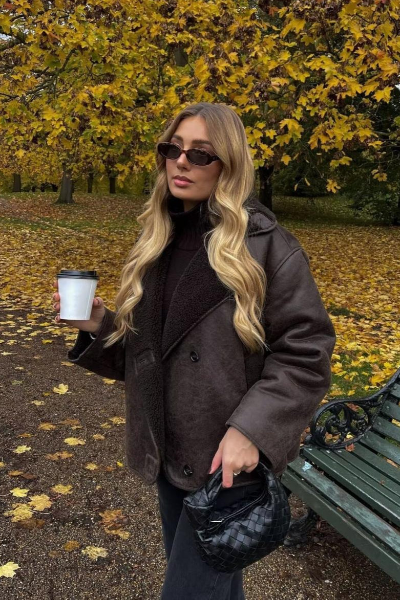 Tessa Brown faux suede jacket styled over a dark turtleneck with a faux shearling collar in an autumn park.