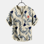 Hanging view of the Vintage Fish-Print Linen Shirt in beige, showcasing the relaxed fit, short sleeves, band collar, and all-over fish print. Designed by Bella Hudson.