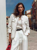Vivienne White textured round-neck jacket with fringe trim and flap pockets, styled open over a satin top and wide-leg trousers on a sunny street.