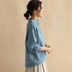 Side view of the Wilhelmina Blouse Draped High-Neck Long-Sleeve in Blue, showcasing its relaxed draped fit and long sleeves.