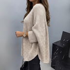 Side view of the Wilhelmine Sweater Oversized Batwing-Sleeve in beige, showcasing the wide batwing sleeves, textured knit fabric, loose drape, and oversized silhouette. Designed by Bella Hudson.