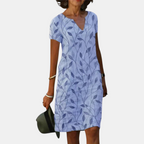Front view of the Winnie Shift Dress Leaf-Print Lightweight Short-Sleeve in blue, featuring a V-neckline, short sleeves, side pockets, and an all-over leaf print. Designed by Bella Hudson.