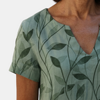 Close-up detail of the Winnie Shift Dress Leaf-Print Lightweight Short-Sleeve in green, featuring the V-neckline, soft lightweight fabric, and botanical leaf print. Designed by Bella Hudson.