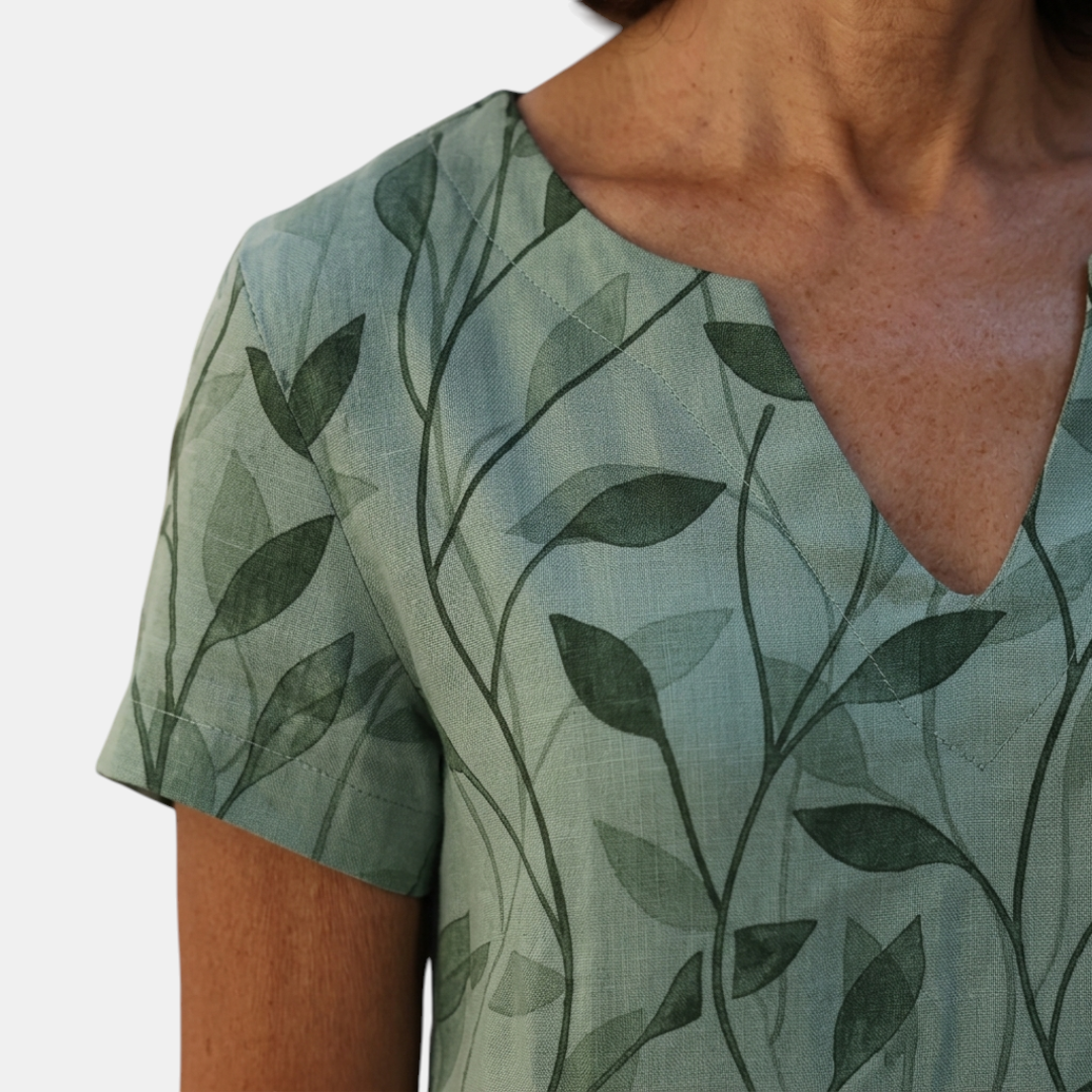 Close-up detail of the Winnie Shift Dress Leaf-Print Lightweight Short-Sleeve in green, featuring the V-neckline, soft lightweight fabric, and botanical leaf print. Designed by Bella Hudson.