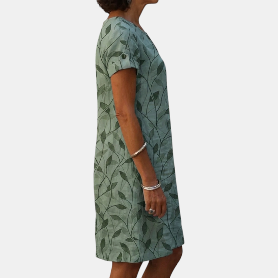 Side view of the Winnie Shift Dress Leaf-Print Lightweight Short-Sleeve in green, showcasing the relaxed fit, short sleeves, side pockets, and lightweight leaf-print fabric. Designed by Bella Hudson.
