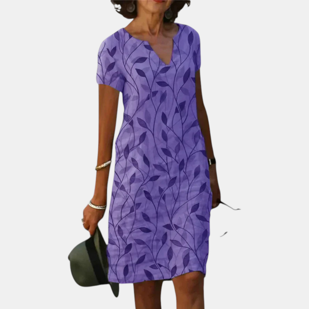 Front view of the Winnie Shift Dress Leaf-Print Lightweight Short-Sleeve in purple, featuring a V-neckline, short sleeves, practical side pockets, and a relaxed shift silhouette with a botanical leaf print. Designed by Bella Hudson.