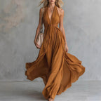 Front view of the Winnifred Maxi Dress Halter Open-Back in dark brown, featuring a plunging V-neckline, halter-style bodice, defined waist, side pockets, and a flowing floor-length silhouette. Designed by Bella Hudson.