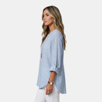 Side view of the Women's Boho Lightweight Blouse in blue, showcasing the relaxed silhouette, rolled sleeves, and flowing high-low hem for effortless everyday style. Designed by Bella Hudson.