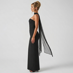 Side view of the Women's Cocktail Maxi Dress Bodycon Fit with Styled Scarf in black, showcasing the sleek bodycon fit, strapless neckline, and flowing sheer scarf detail. Designed by Bella Hudson.
