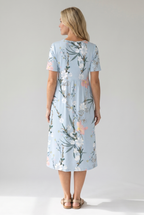 Back view of light blue floral print midi dress with short sleeves and flowing midi silhouette by BELLA HUDSON